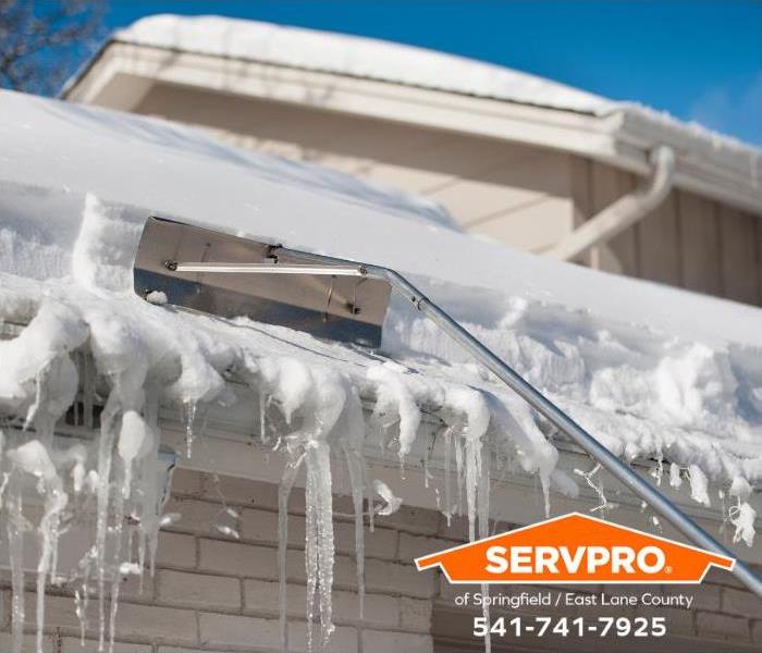 A person uses a roof rake to remove ice dams and snow.